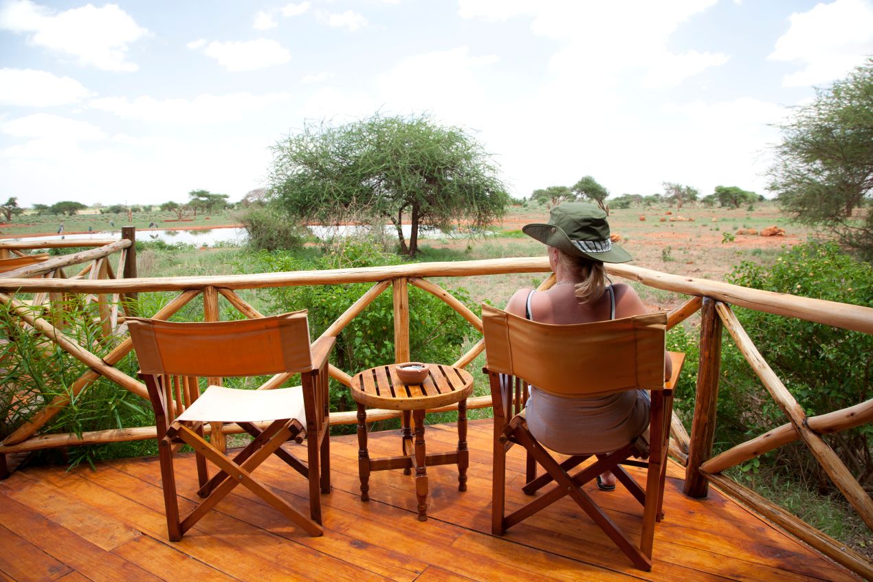 Frau auf einer Holzterrasse mit Blick auf die weite Savanne während einer Tansania Safari